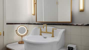 A bathroom with a white sink, gold faucets, and a round mirror with a light.