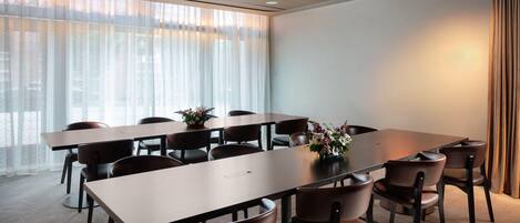 A conference room with a long table and chairs, large windows with sheer curtains, and a carpeted floor.