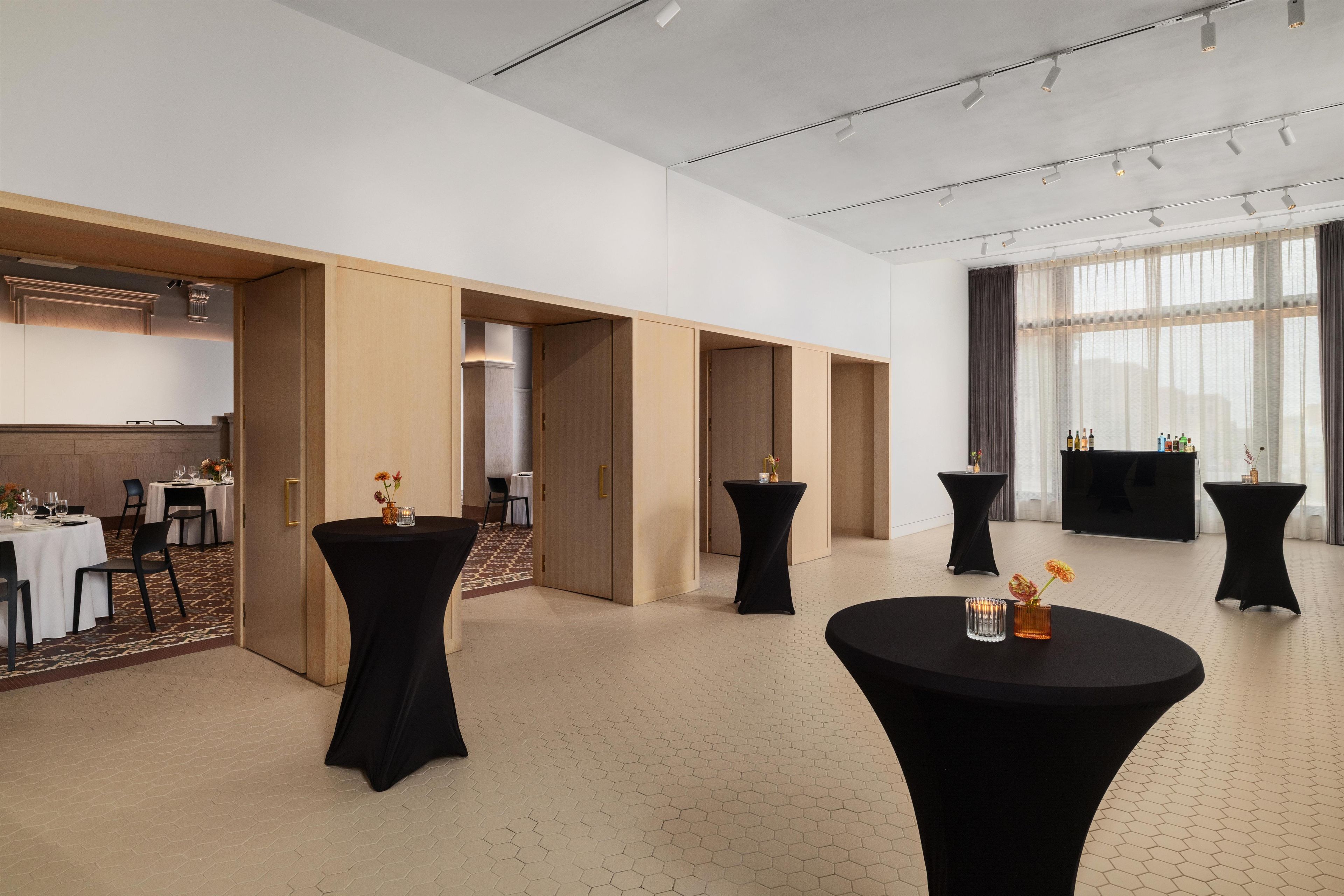 Un hall d’hôtel doté de plusieurs tables rondes, d’un comptoir d’accueil et offrant une vue sur l’extérieur grâce à de grandes fenêtres.