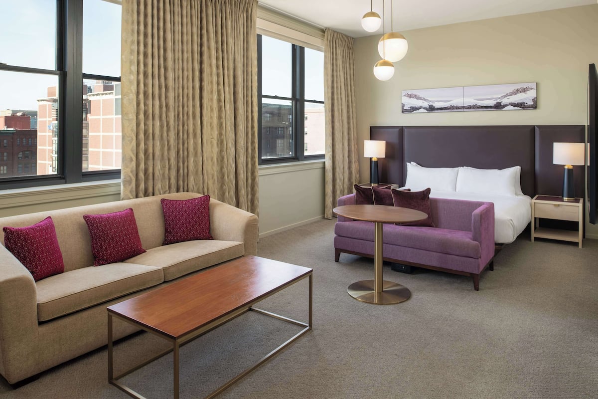 Une chambre d’hôtel avec un canapé, une table ronde, un lit et une table de chevet avec une lampe.