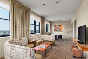 Quarto de hotel com sofá, mesa de jantar, televisão e vista para a cidade.
