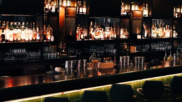 Un bar doté de plusieurs étagères remplies de bouteilles et de verres, d’un comptoir et de tabourets de bar.