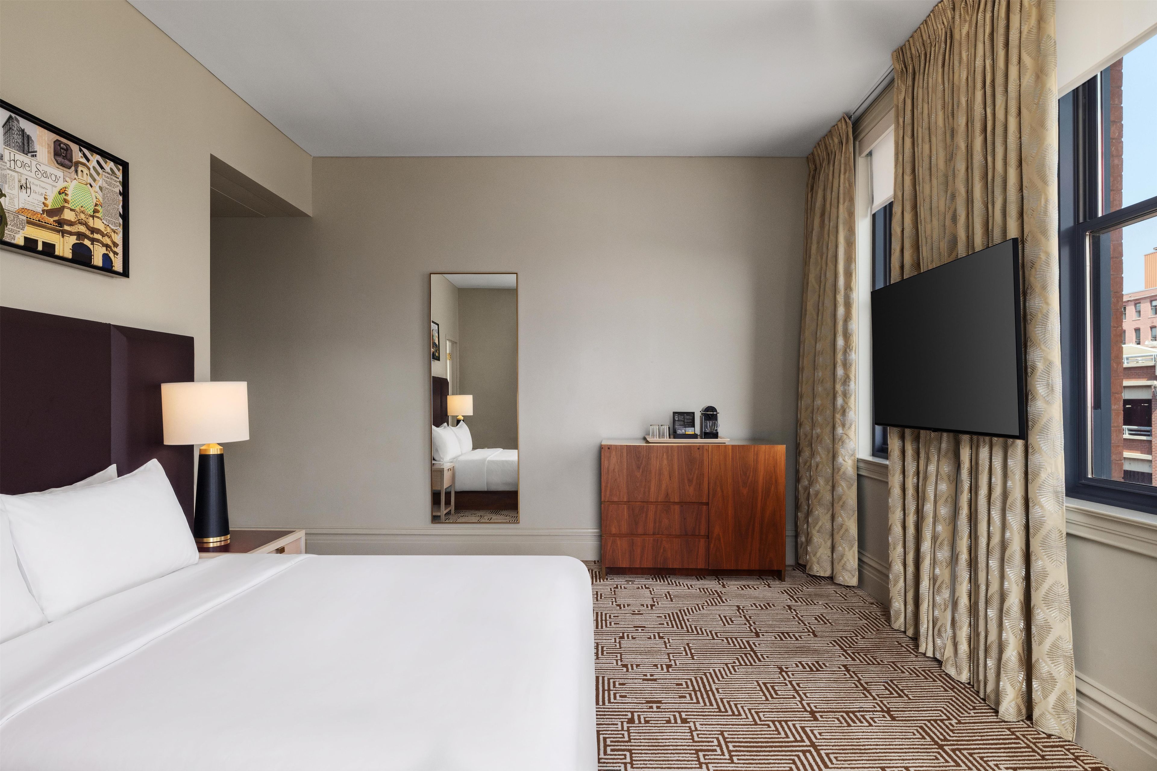 Una habitación de hotel con una cama grande, un televisor de pantalla plana, un aparador de madera y una alfombra estampada.