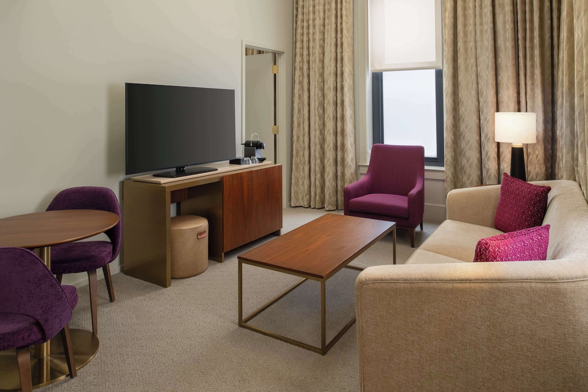 Une chambre d’hôtel équipée d’une télévision, d’un bureau, de fauteuils violets, d’un canapé et d’une lampe.