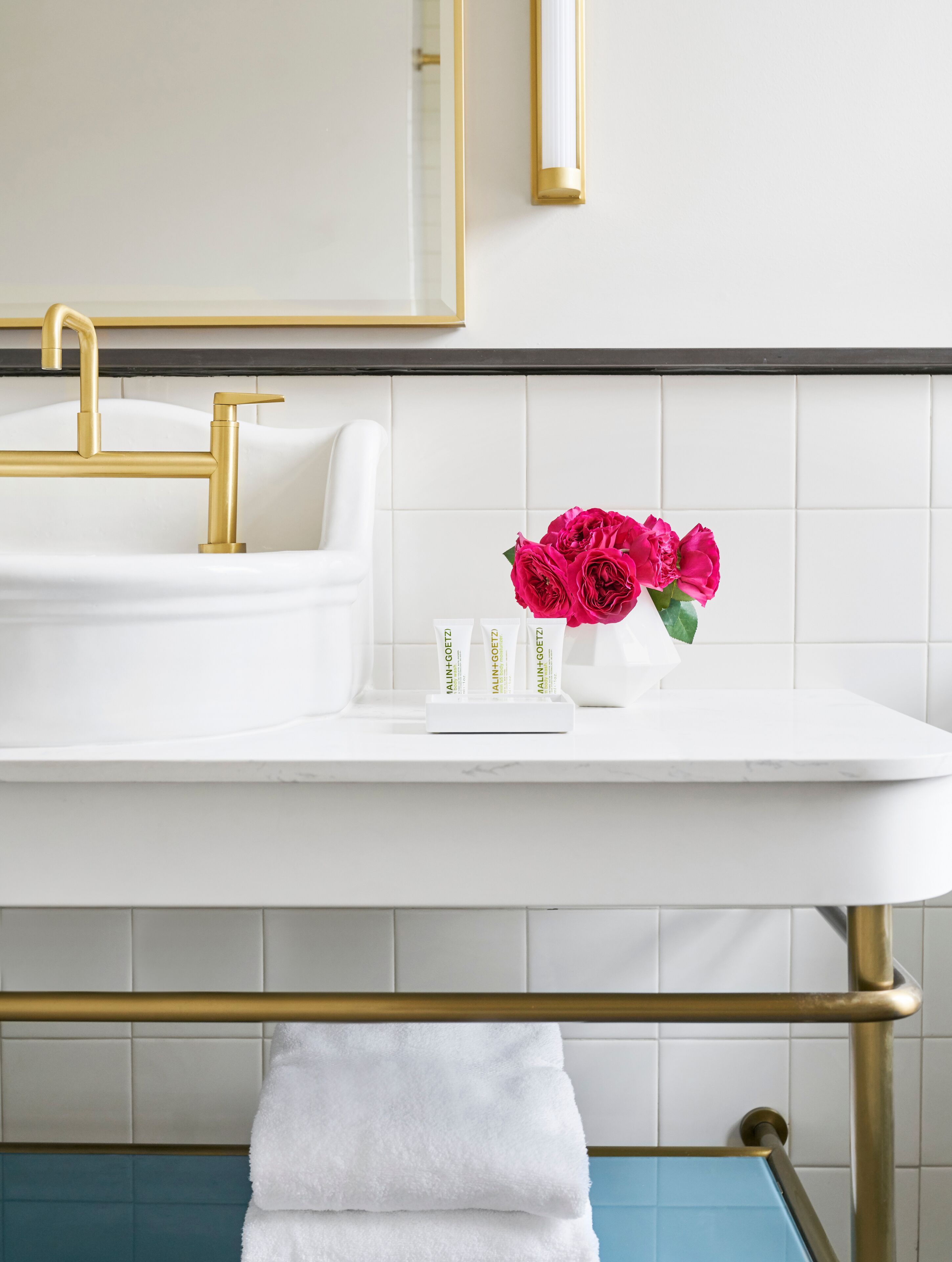 A bathroom with a white sink, gold fixtures, and a vase with pink flowers on the counter.