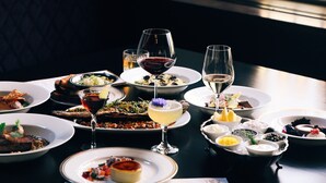 Une table à manger dressée avec différents plats et verres, un menu, et une fenêtre avec des vitres à croisillons.