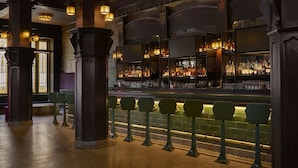 A bar area with a counter, stools, and a variety of bottles and glasses. - Hotel Savoy Kansas City, Tapestry Collection by Hilton (Kansas City)