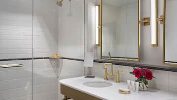 A modern bathroom with a glass-enclosed shower, two sinks with gold fixtures, and a large mirror with gold trim.