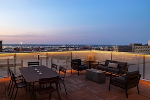 Un espace extérieur aménagé avec des sièges, offrant une vue sur les toits de la ville au crépuscule.
