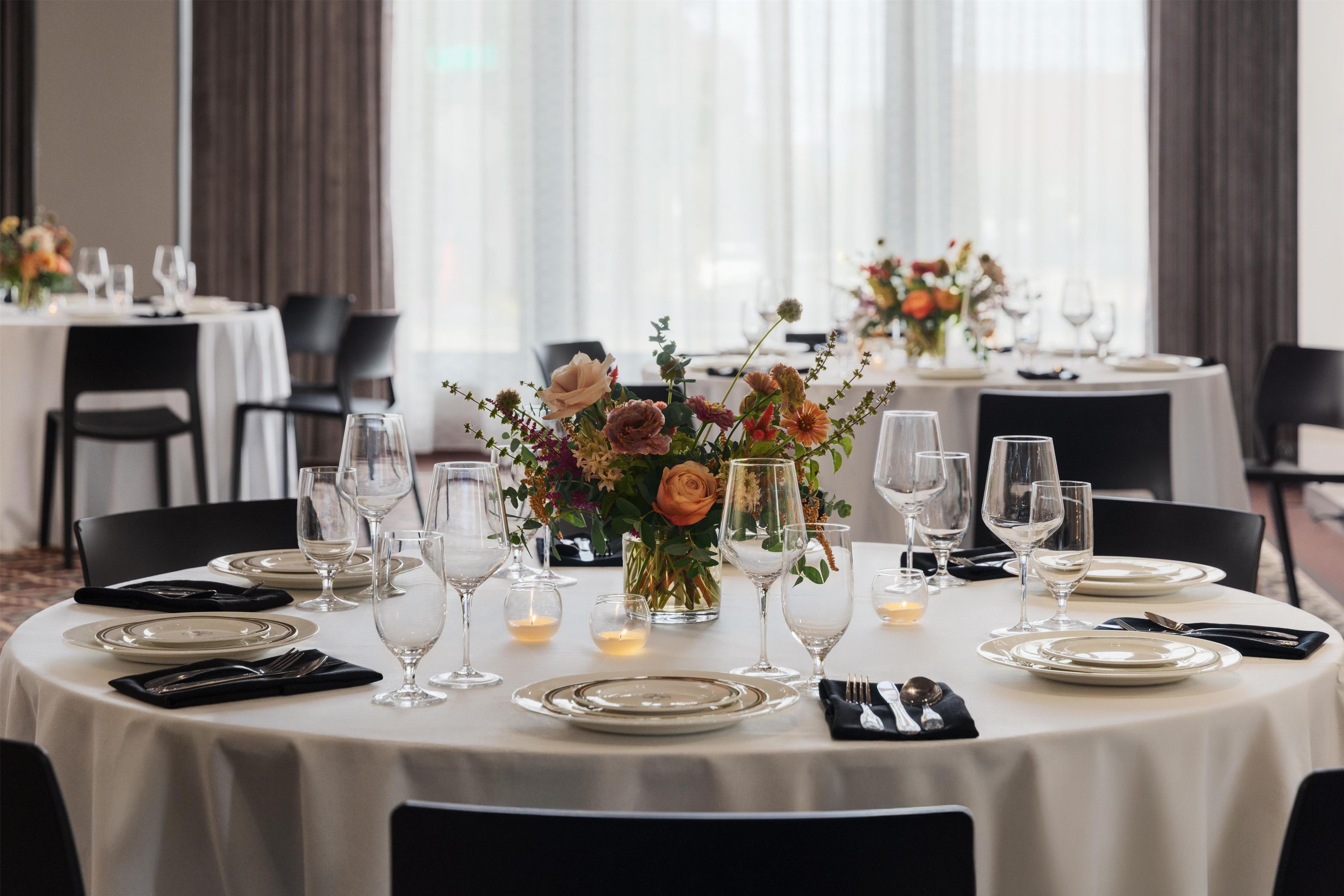 Un restaurant avec des tables rondes, chacune mise avec des assiettes, des couverts et des verres à vin.