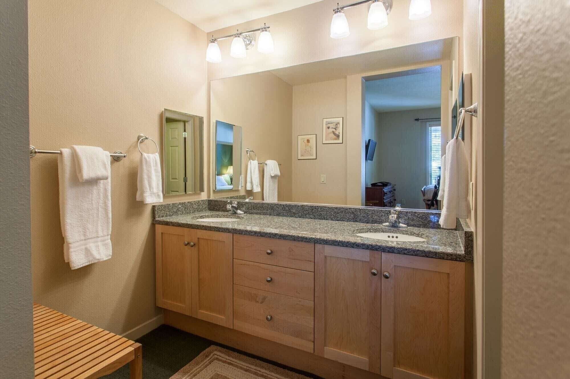 Een badkamer met twee wastafels, houten kastjes, een spiegel en een handdoekrek.