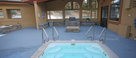 A covered outdoor swimming pool with a stone bench and a grill area.
