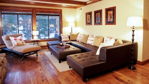 Una sala de estar con un sofá modular, una tumbona y una mesa de centro. Hay dos lámparas de pie y tres marcos de cuadros en la pared.