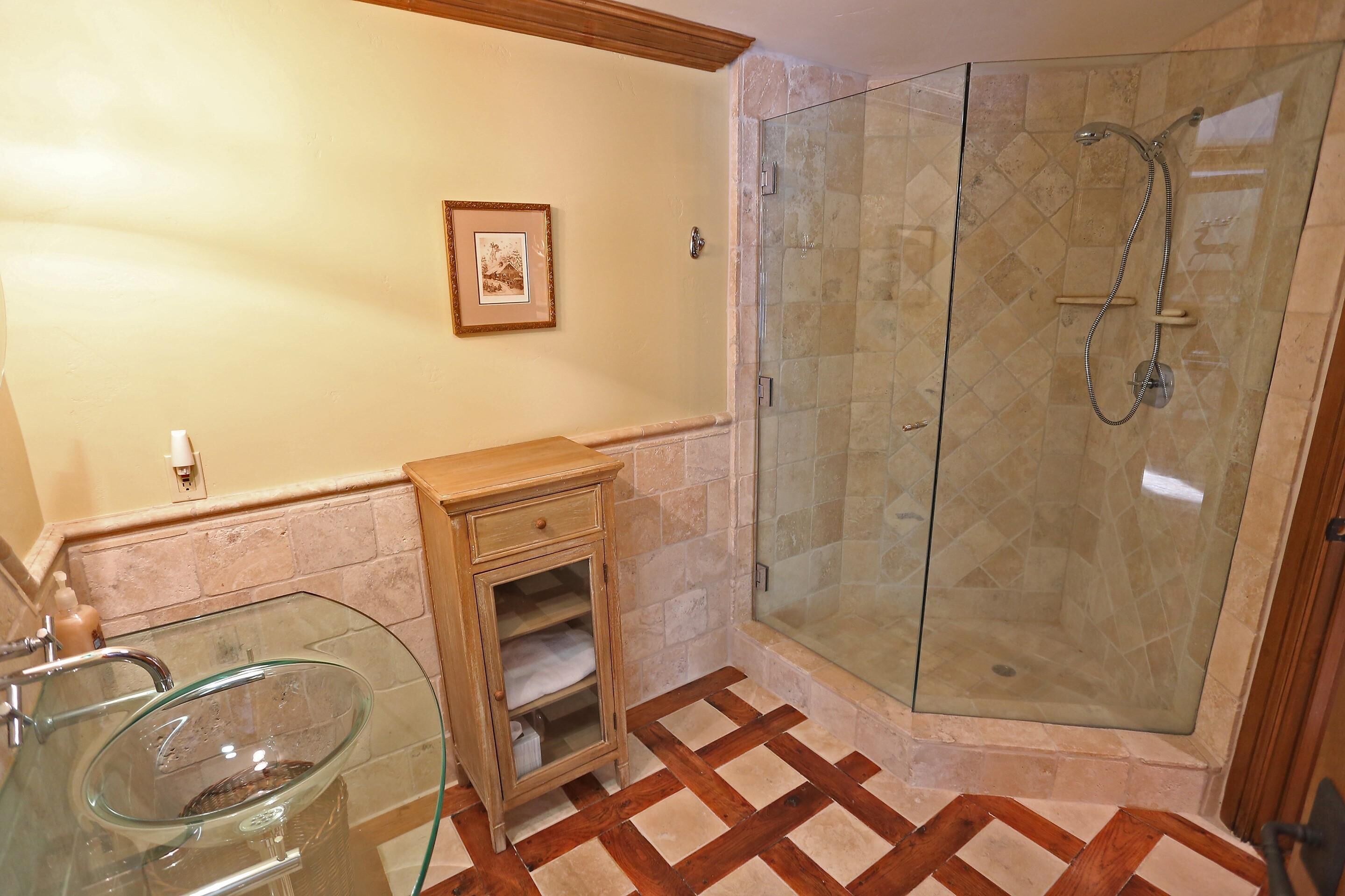A bathroom with a glass-enclosed shower, a glass sink, and a wooden cabinet.