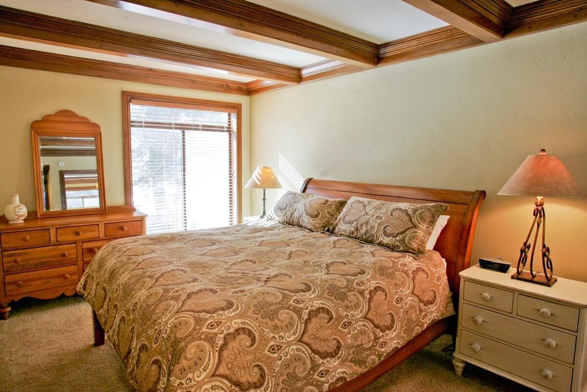 A bedroom with a large bed, wooden headboard, a dresser, a mirror, and a bedside lamp.