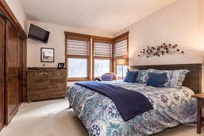 A bedroom with a large bed, wooden dresser, and a TV mounted on the wall. - Snowcreek 883 Phase V (Mammoth Lakes)