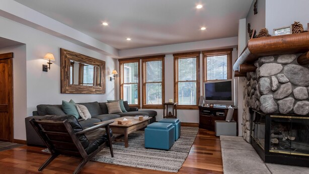 A modern living room with a stone fireplace, wooden flooring, and a large sectional sofa. - Snowcreek 883 Phase V (Mammoth Lakes)