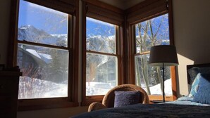 A bedroom with a bed, a chair, and a lamp. There are three windows with a view of snow-covered mountains. - Snowcreek 883 Phase V (Mammoth Lakes)