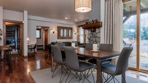 A dining area with a wooden table and chairs, a stone accent wall, and a view of the outdoors. - Snowcreek 883 Phase V (Mammoth Lakes)