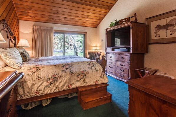 A bedroom with a wooden ceiling, a bed with floral bedding, a dresser, and a television. - Snowcreek 320 Phase 2 (Mammoth Lakes)