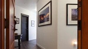 A hallway with wooden flooring, white walls, and framed pictures on the walls.