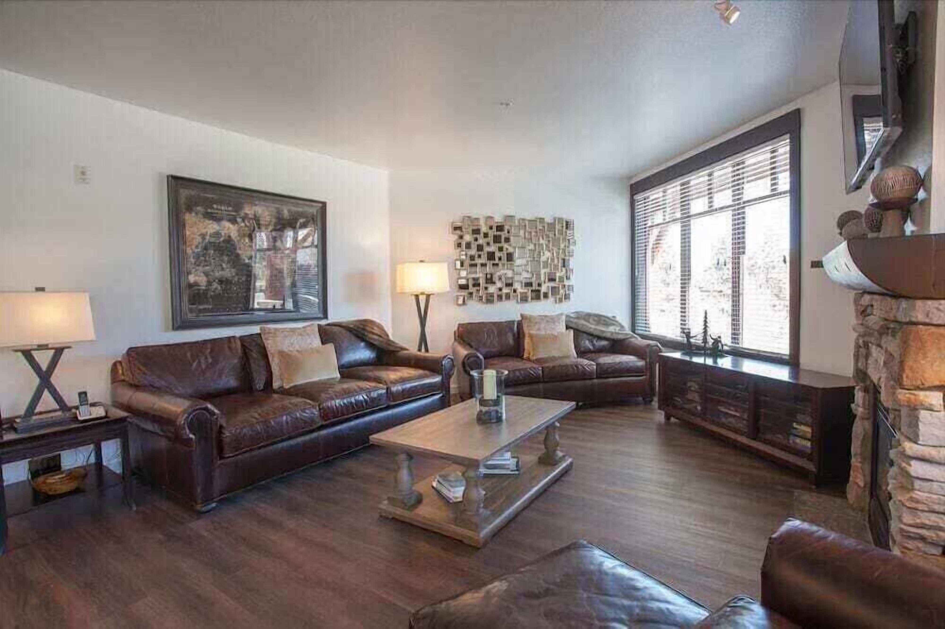 A living room with dark wood flooring, leather sofas, a coffee table, and a stone fireplace.