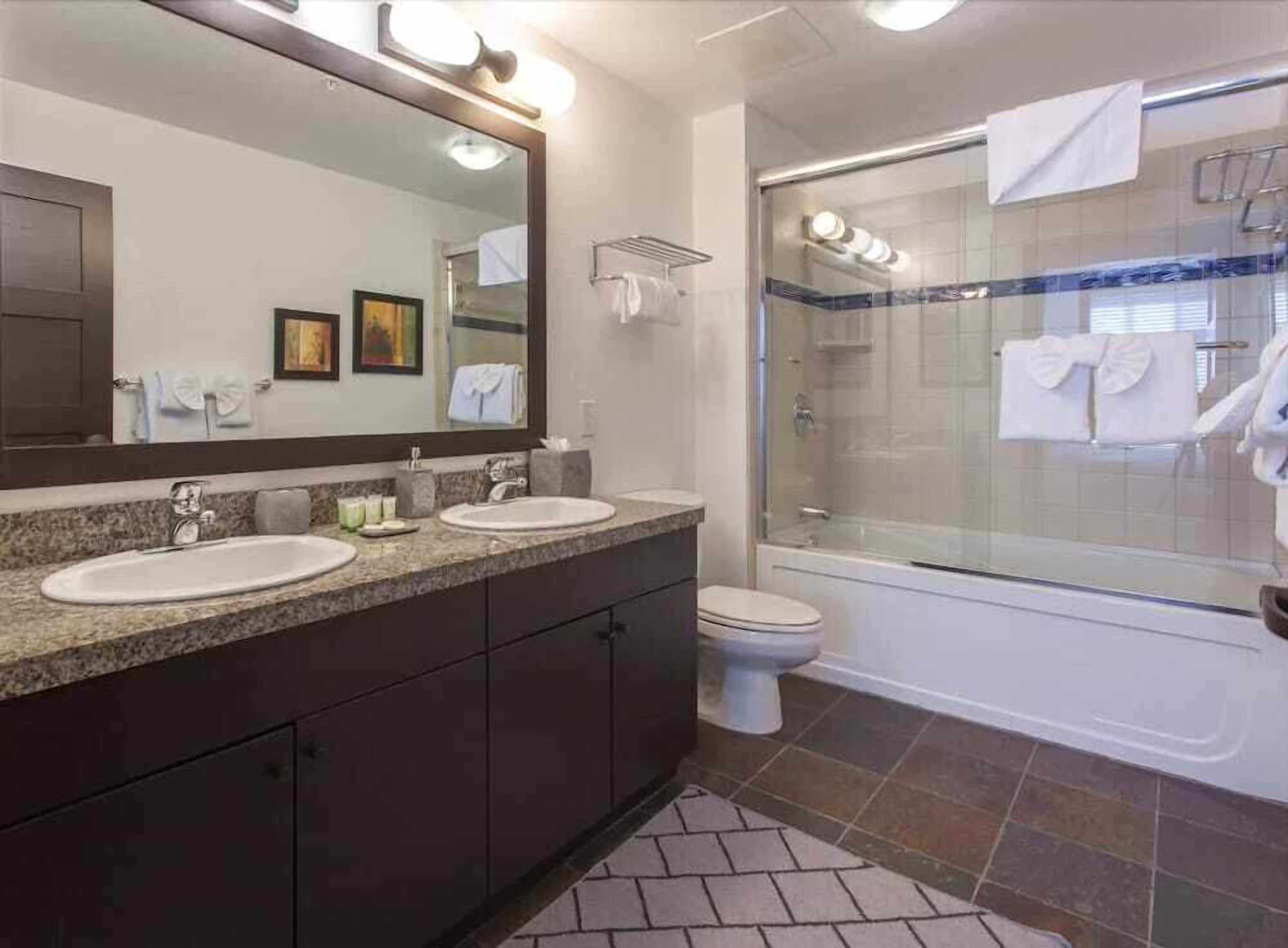 A modern bathroom with two sinks, a large mirror, a shower enclosure, and a toilet.
