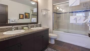 A modern bathroom with two sinks, a large mirror, a shower enclosure, and a toilet.