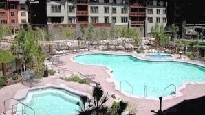A resort with multiple swimming pools, a landscaped area with rocks and plants, and a multi-story building with balconies.