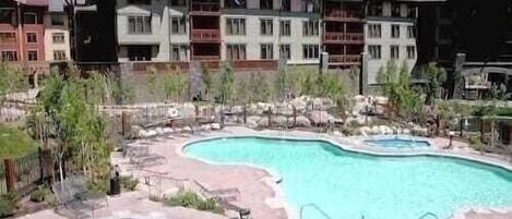 A resort with multiple swimming pools, a landscaped area with rocks and plants, and a multi-story building with balconies.