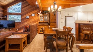 A cozy cabin interior with a wooden dining table, chairs, a sofa, and a television. - Snowflower 62 (Mammoth Lakes)