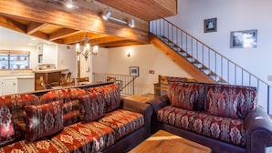 A spacious living area with a wooden ceiling, a staircase, and a kitchen in the background. - Snowflower 62 (Mammoth Lakes)