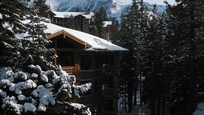 A lodge with a wooden exterior, surrounded by snow-covered trees and mountains in the background. - Val d'lsere 21 (Mammoth Lakes)