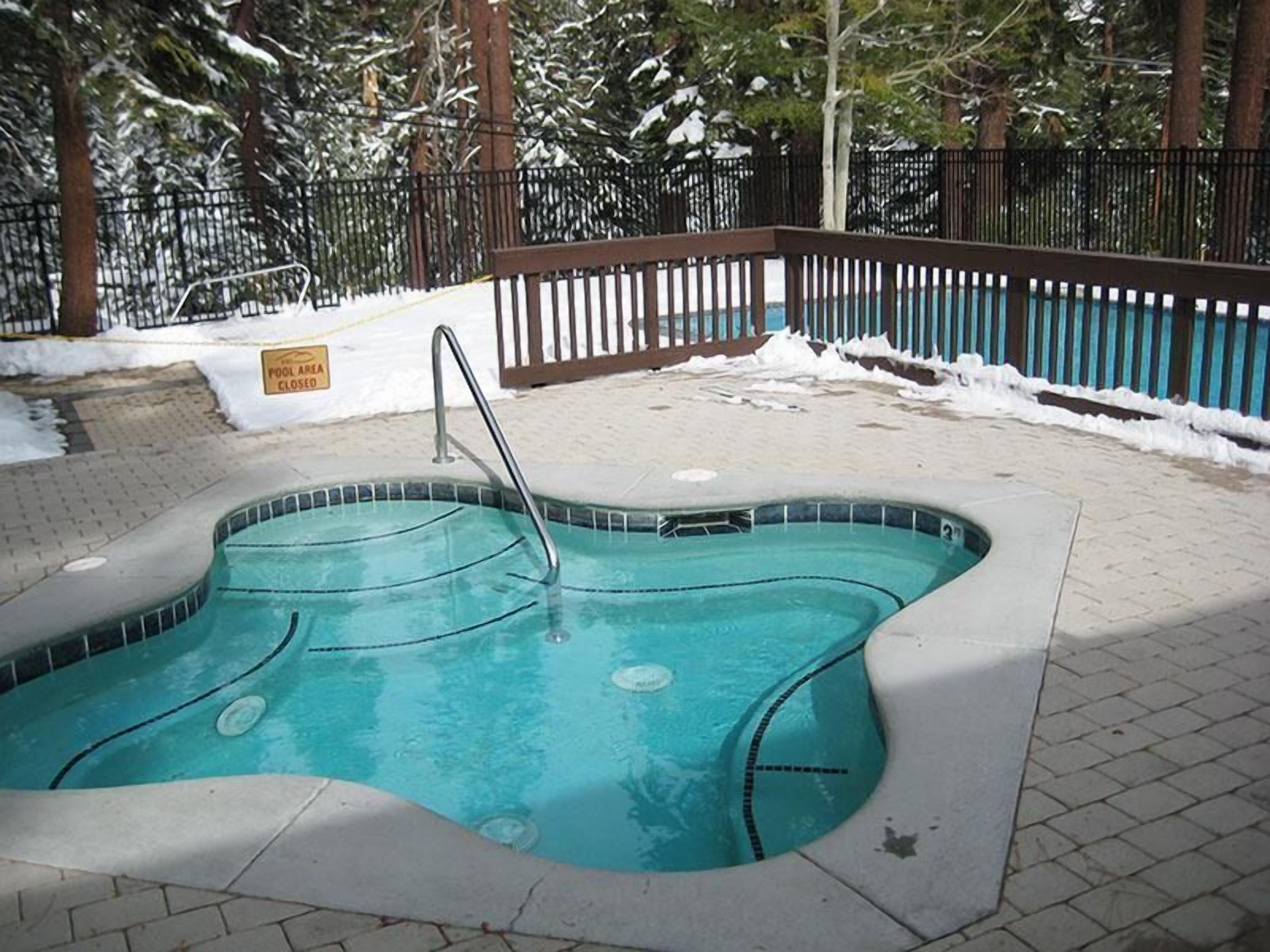 A swimming pool with a metal ladder, surrounded by a brick deck and a wooden fence.