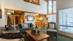 A spacious living room with a high ceiling, a fireplace, and a view of the kitchen. - Val d'lsere 21 (Mammoth Lakes)