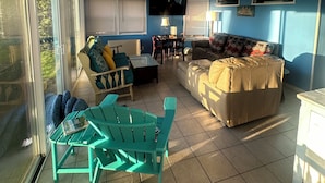 Een woonkamer met een bank, stoelen, een televisie en een eettafel.