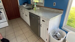 Een keuken met witte kastjes, een spoelbak en een raam.