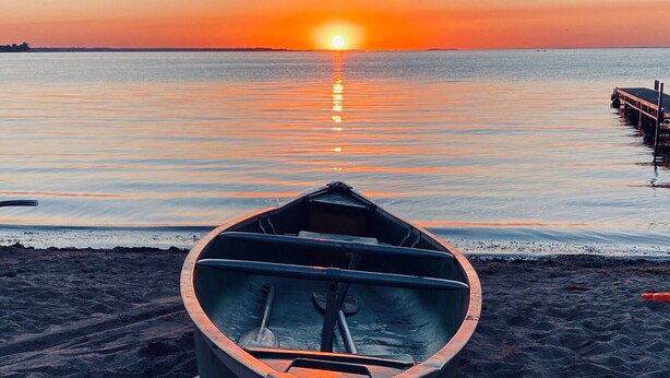Een roeibootje op een zanderig strand met een ondergaande zon op de achtergrond.