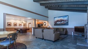 A spacious living area with a stone floor, a dining table with chairs, a sofa, a fireplace, and a kitchen in the background. - Chamonix 92 (Mammoth Lakes)