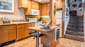 A kitchen with wooden cabinets, a microwave, a sink, and a bar stool. - Chamonix 92 (Mammoth Lakes)