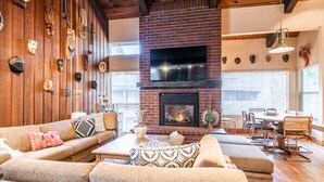 A cozy living room with a brick fireplace, wooden walls, and a variety of decorative masks. - Chamonix 92 (Mammoth Lakes)