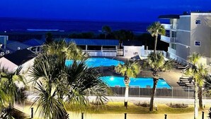 Ein Swimmingpool, umgeben von Palmen und einem Gebäude mit Balkonen mit Blick auf den Ozean.