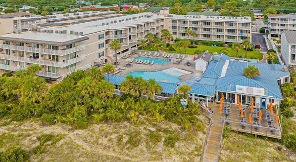 A hotel with multiple floors, a swimming pool, and a beach area with umbrellas.