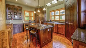 A spacious kitchen with wooden cabinets, a central island with stools, and a large window providing natural light.