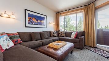 A modern living room with a sectional sofa, a wooden coffee table, and a large window with curtains.
