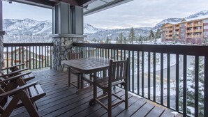 Eine Holzterrasse mit Tisch und Stühlen mit Blick auf eine verschneite Berglandschaft und ein Gebäude mit Balkonen.