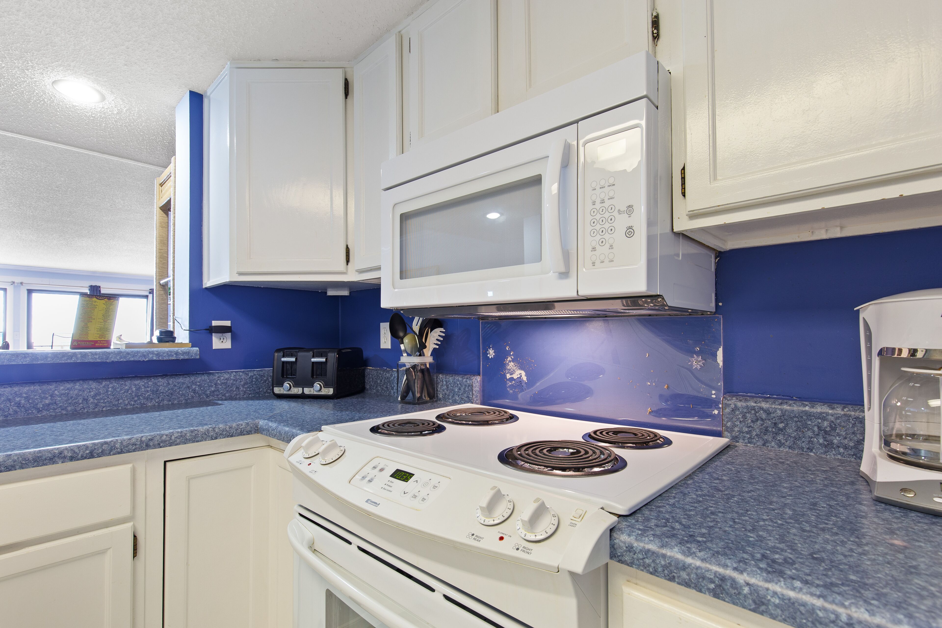 A kitchen with white cabinets, a white stove, a microwave, and a blue countertop.