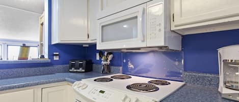 A kitchen with white cabinets, a white stove, a microwave, and a blue countertop.