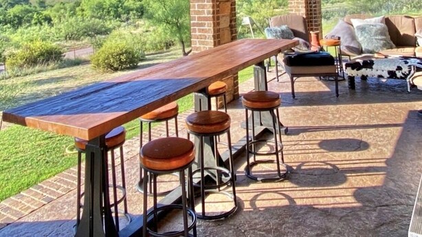 An outdoor patio with a long wooden table and bar stools, a ceiling fan, and a view of a hilly landscape. - The LonePine in YellowHouse Canyon (Slaton)