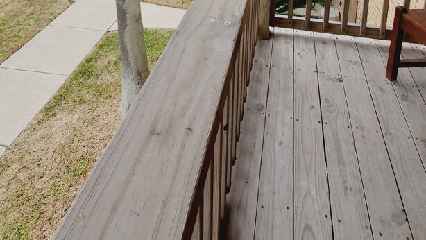 Une terrasse en bois avec une balustrade, une vue sur une étendue d’eau et un bâtiment à la façade en briques.